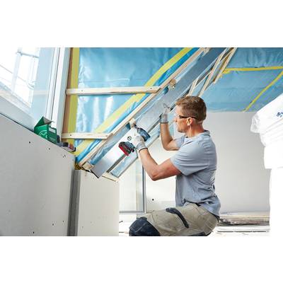 Ein Mann arbeitet an einer Dachkonstruktion in einem Gebäude, trägt Schutzkleidung und benutzt Werkzeuge für den Innenausbau.