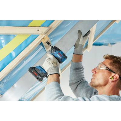 Mann installiert Metallträger an einer Dachkonstruktion, trägt Schutzbrille und Handschuhe. Verwenden eines elektrischen Bohrers.