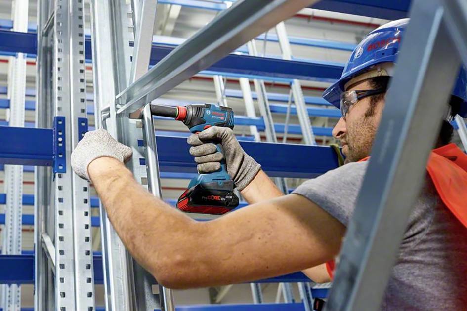 Ein Bauarbeiter in Schutzkleidung montiert ein Metallregal mit einem Akkuschrauber in einem Lager.