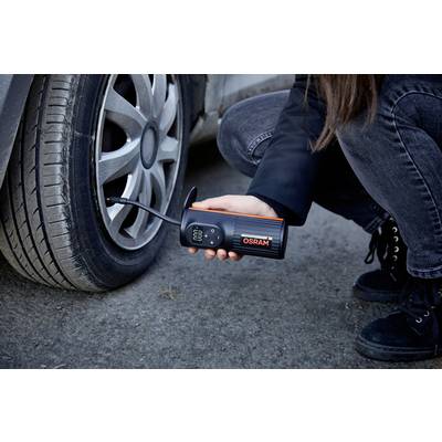 Person überprüft mit einem mobilen Gerät den Reifendruck eines Autos, das auf einer Straße steht.