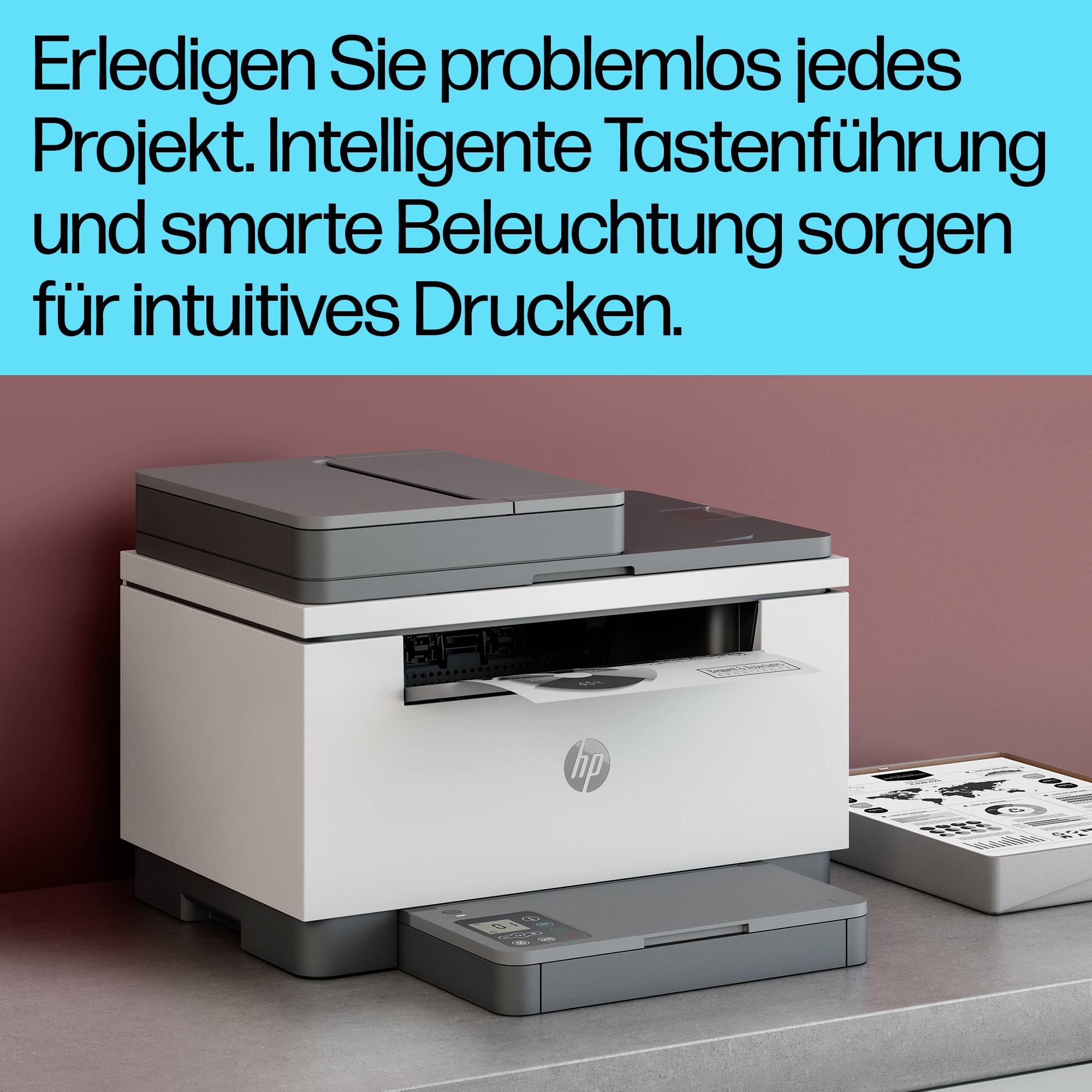 Der Drucker ist auf einem Tisch platziert. Der Text in Blau oben lautet: 'Erledigen Sie problemlos jedes Projekt. Intelligente Tastenführung und smarte Beleuchtung sorgen für intuitives Drucken.'