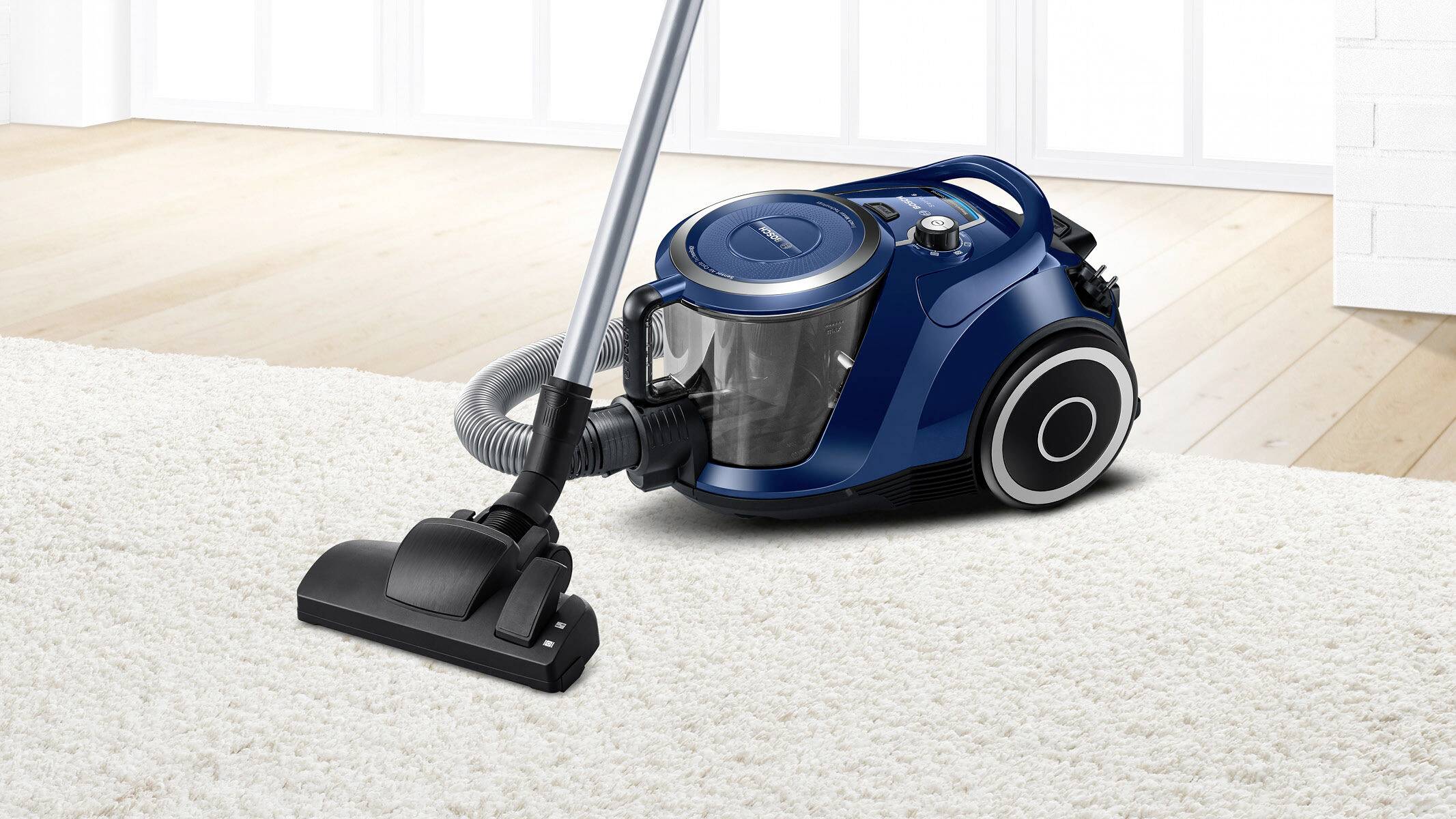 Blauer Staubsauger auf hellem Teppich in einem modernen Raum, zeigt den Staubsauger in Benutzung.