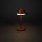 Eine moderne, minimalistische Tischlampe mit rundem Schirm und Sockel leuchtet warmes Licht aus, vor dunklem Hintergrund.