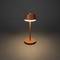 Eine minimalistische Tischlampe mit braunem Schirm leuchtet auf dunklem Hintergrund.