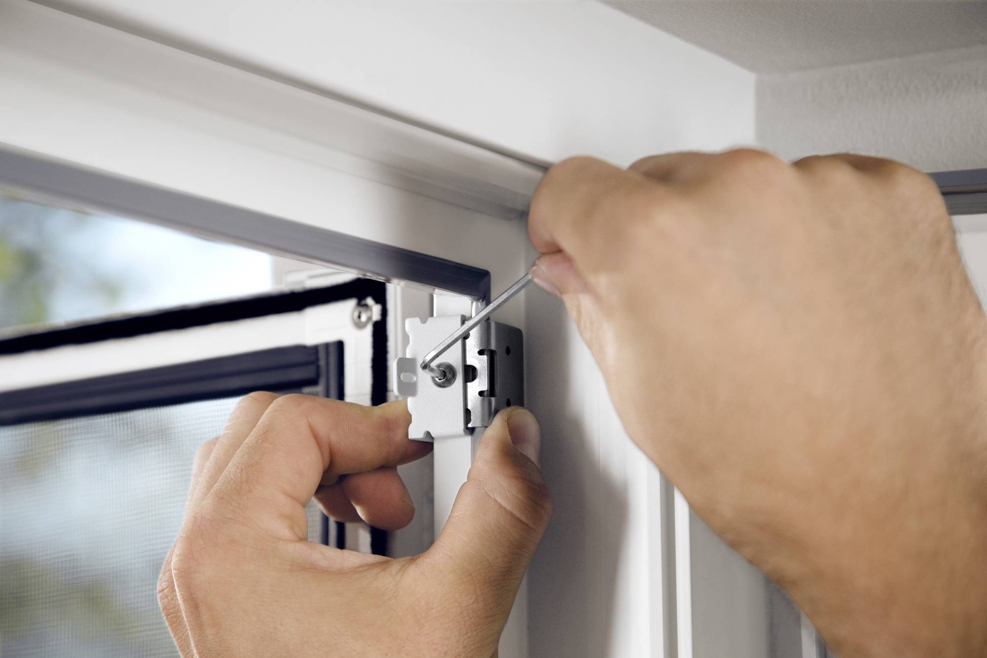 'Eine Person justiert ein Scharnier an einem Fensterrahmen mit einem Schraubenzieher, möglicherweise zur Anpassung der Fensterfunktion.'