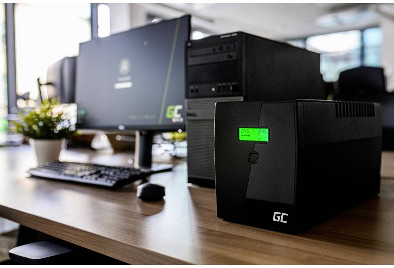 Ein UPS-Gerät steht auf einem Schreibtisch neben einem Computer und Monitor in einem Büro. Es sorgt für Stromabsicherung bei Ausfällen.