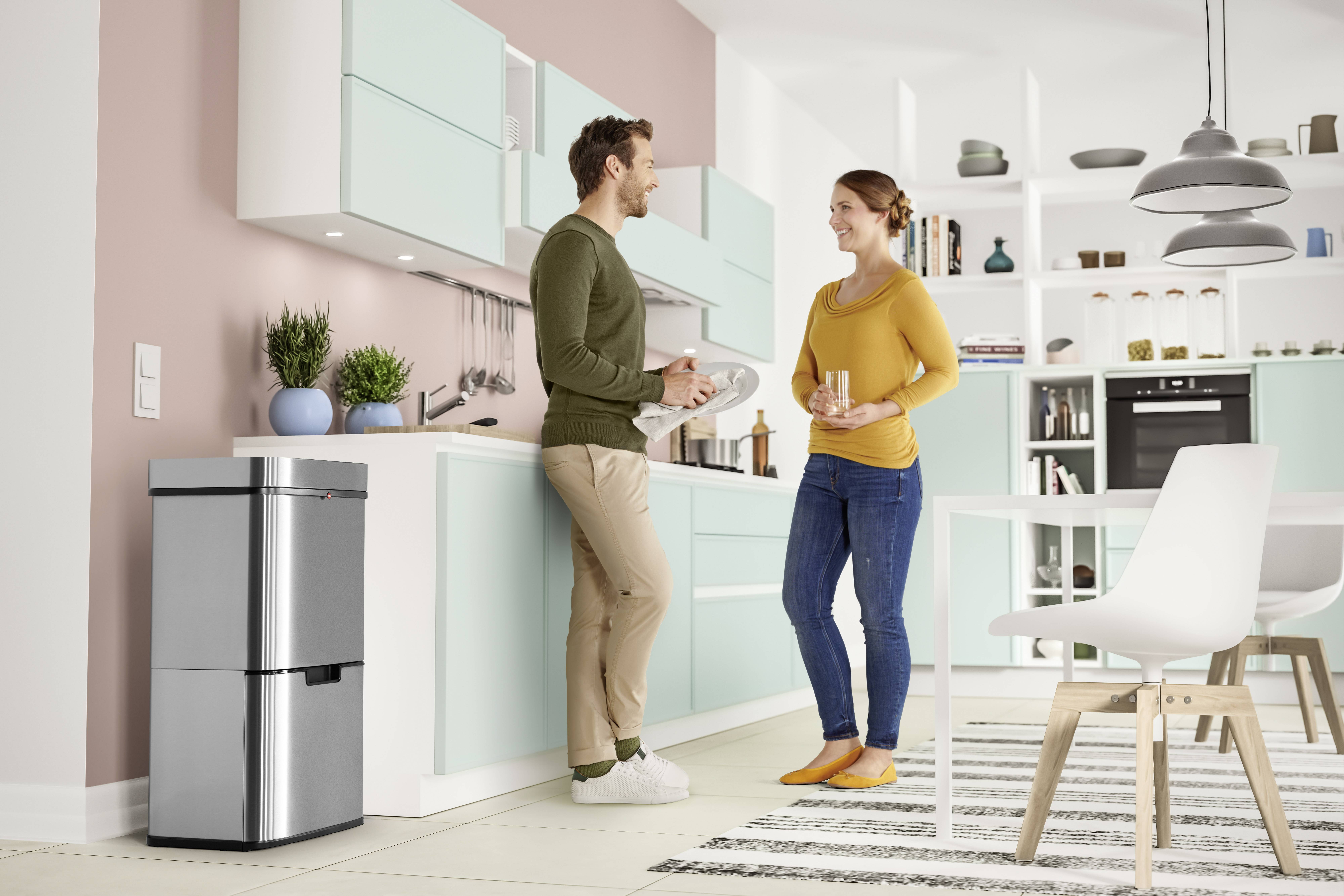 Ein Mann und eine Frau stehen in einer modernen Küche, unterhalten sich und lächeln. Neben ihnen steht ein silberner Mülleimer.