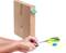 Hände kleben einen blauen Magnet auf einen grünen Papierstreifen, der aus einem aufrechten, verpackten Karton ragt; daneben eine grüne Schere.