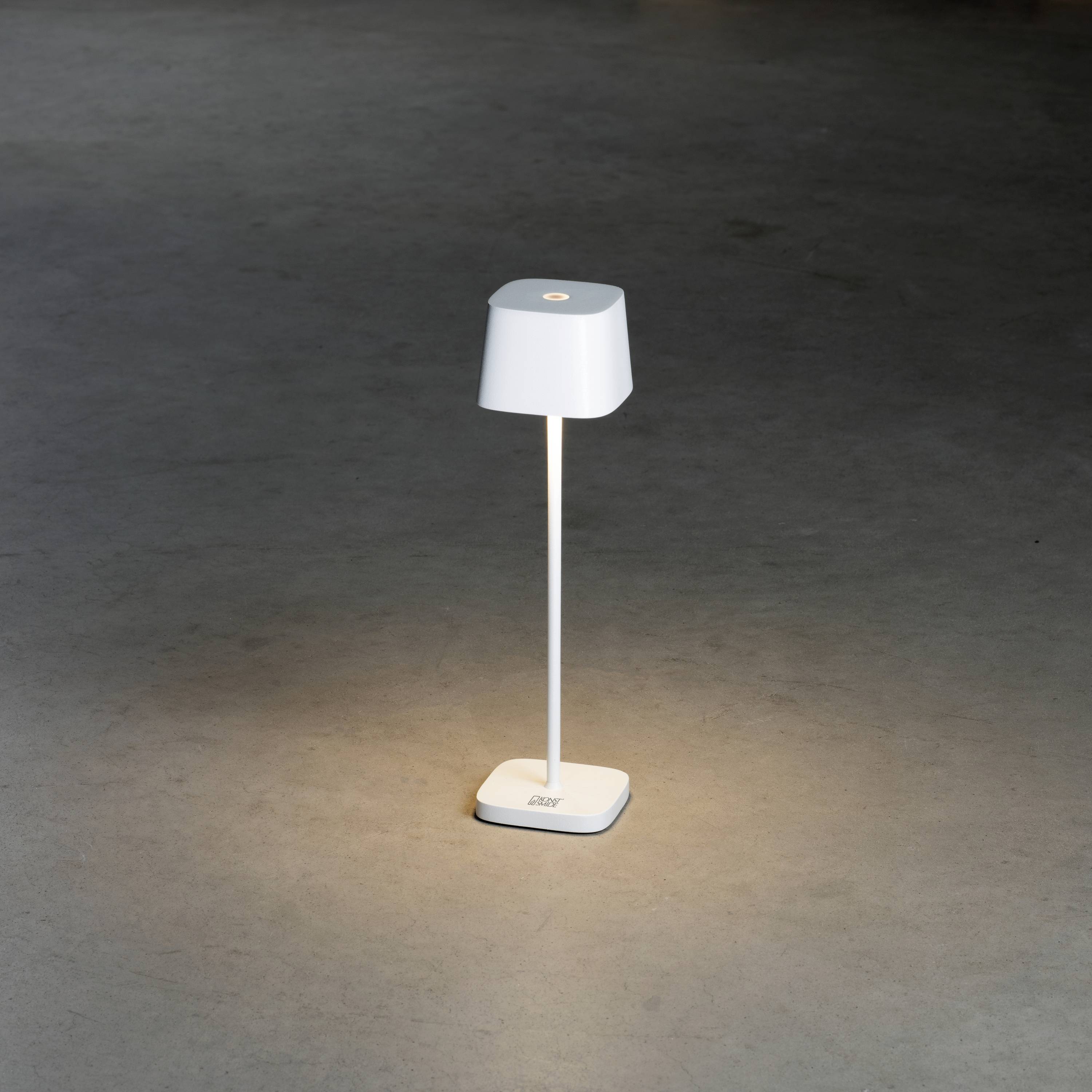 Eine schlanke, weiße Tischlampe leuchtet auf dunklem Untergrund. Die Lampe hat einen minimalistischen, modernen Stil.