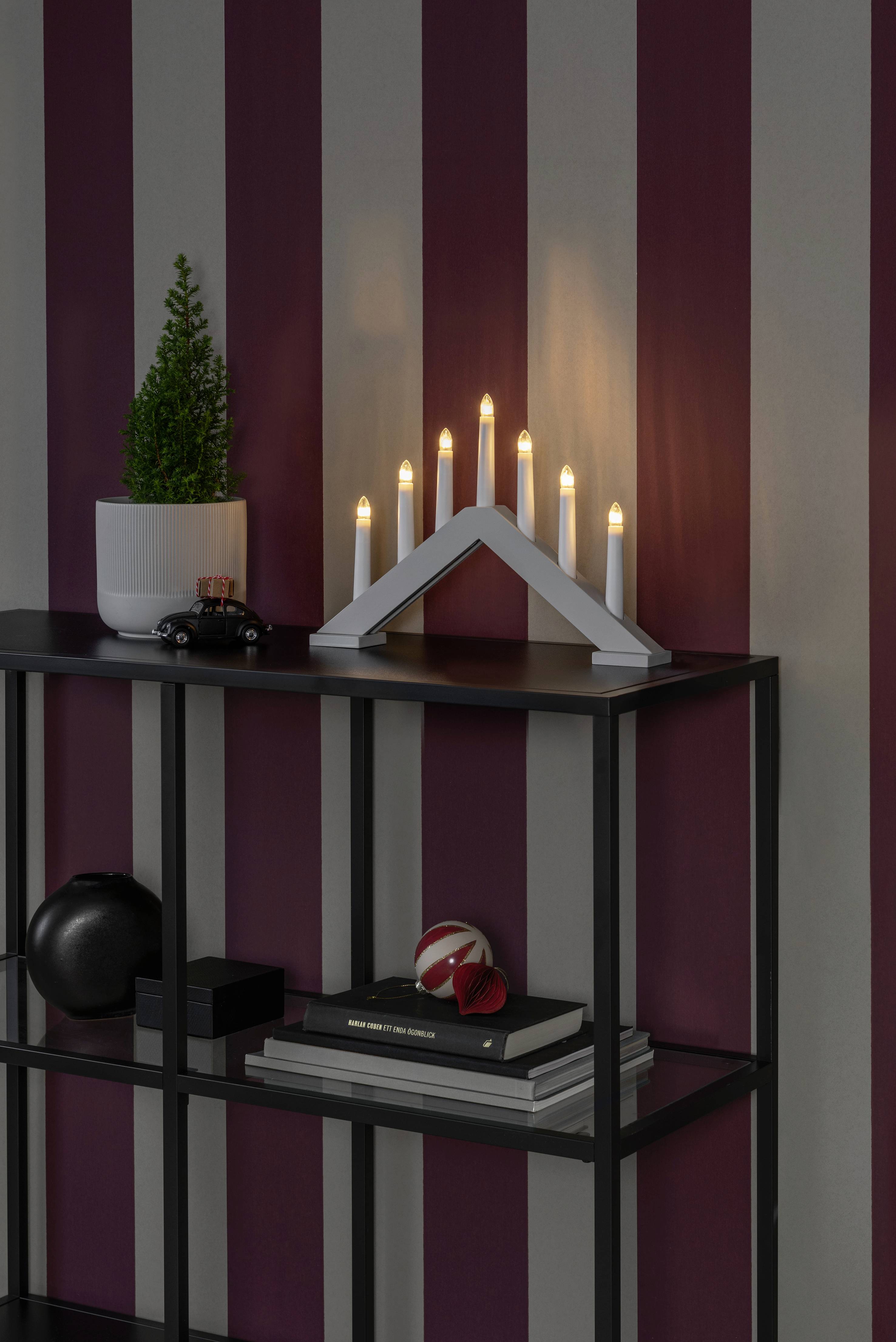 Ein schwarzes Regal vor einer rot-weiß gestreiften Wand. Darauf eine Pflanze im Topf, ein Spielzeugauto und ein beleuchteter Kerzenhalter.