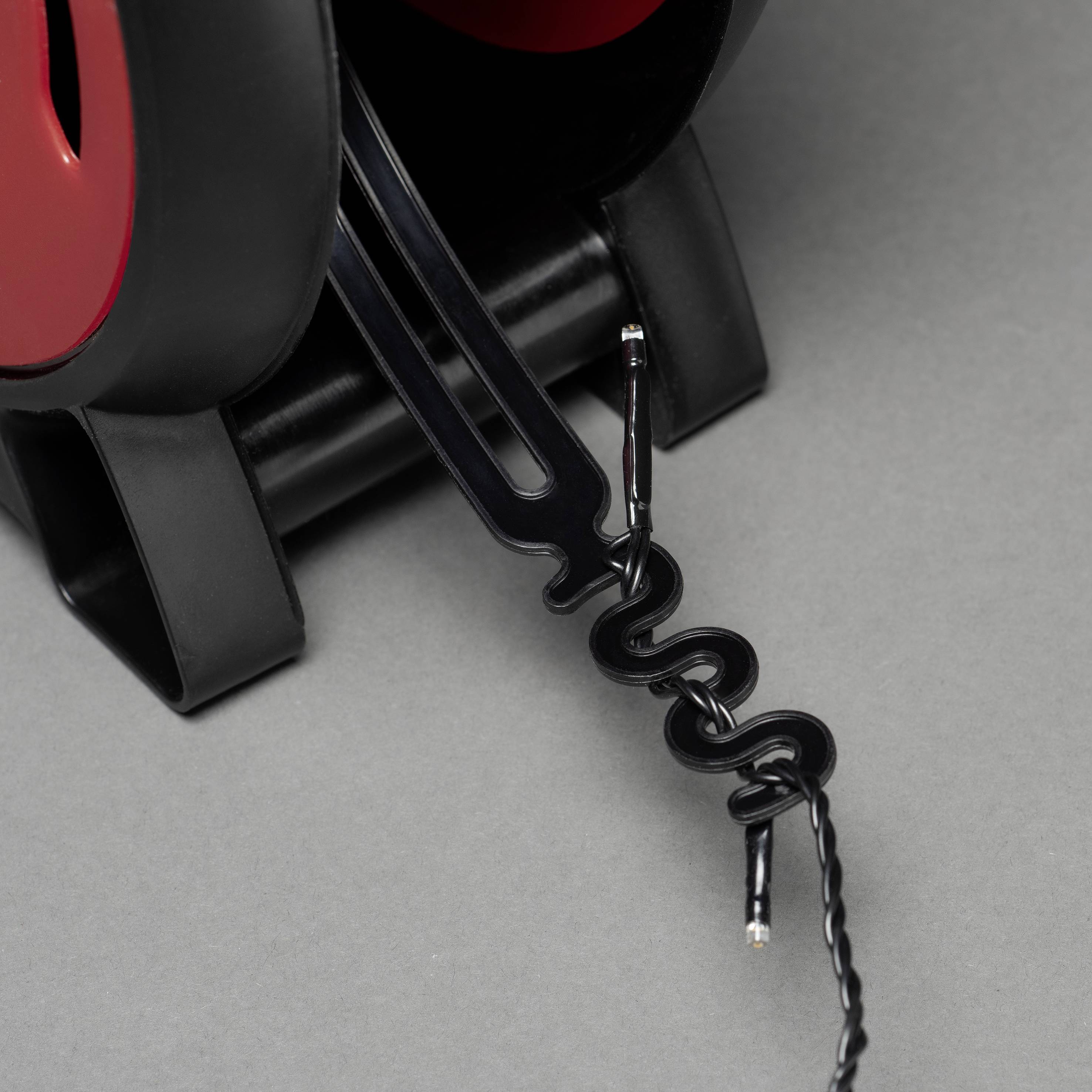 Nahaufnahme eines schwarzen Telefonhörers mit rotem Akzent, auf grauem Hintergrund. Ein verdrilltes Kabel endet in einem offenen Draht.