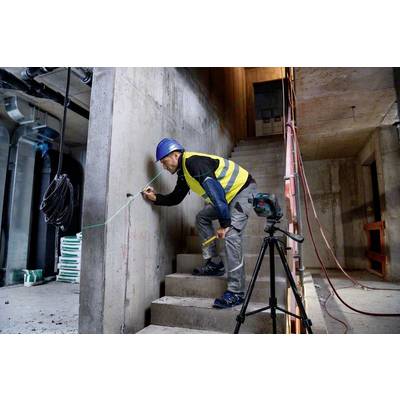 Ein Bauarbeiter in Schutzkleidung misst und markiert eine Betonwand in einem halbfertigen Gebäude mit Ausrüstungen um ihn herum.