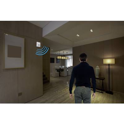Eine Person betritt einen modern eingerichteten Raum. Ein Sensor an der Wand aktiviert eine Lampe, die den Raum beleuchtet.