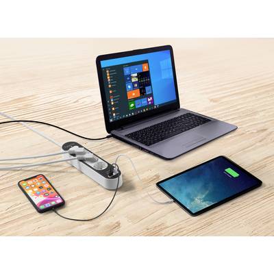 Ein Laptop, ein Tablet und ein Smartphone sind über ein Verlängerungskabel auf einem Holztisch angeschlossen und werden aufgeladen.