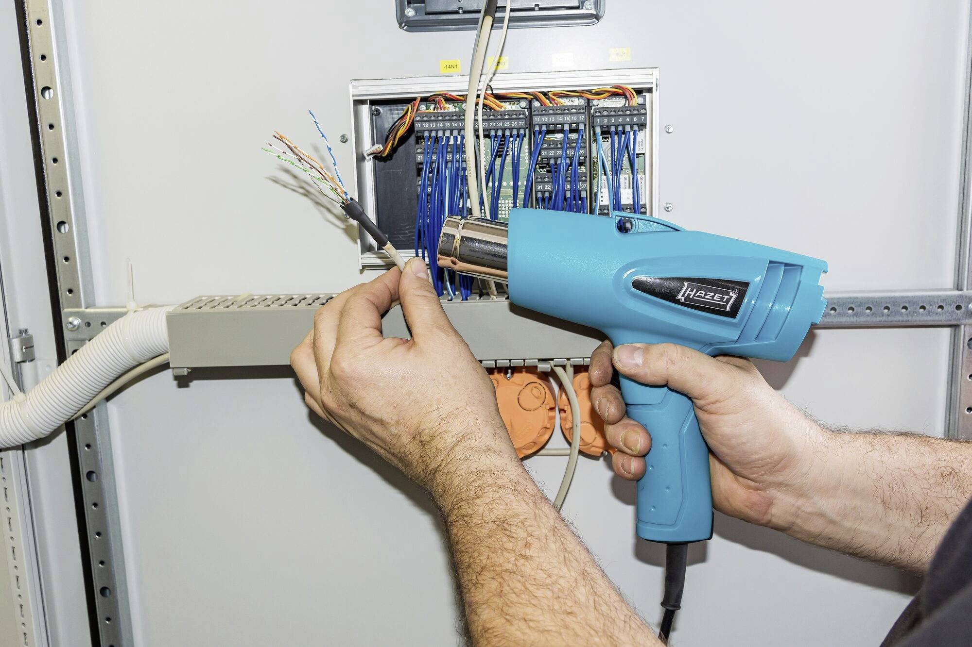 Person verwendet Heißluftfön, um Kabel in einem Verteilerkasten zu bearbeiten. Elektrische Installationsarbeit.