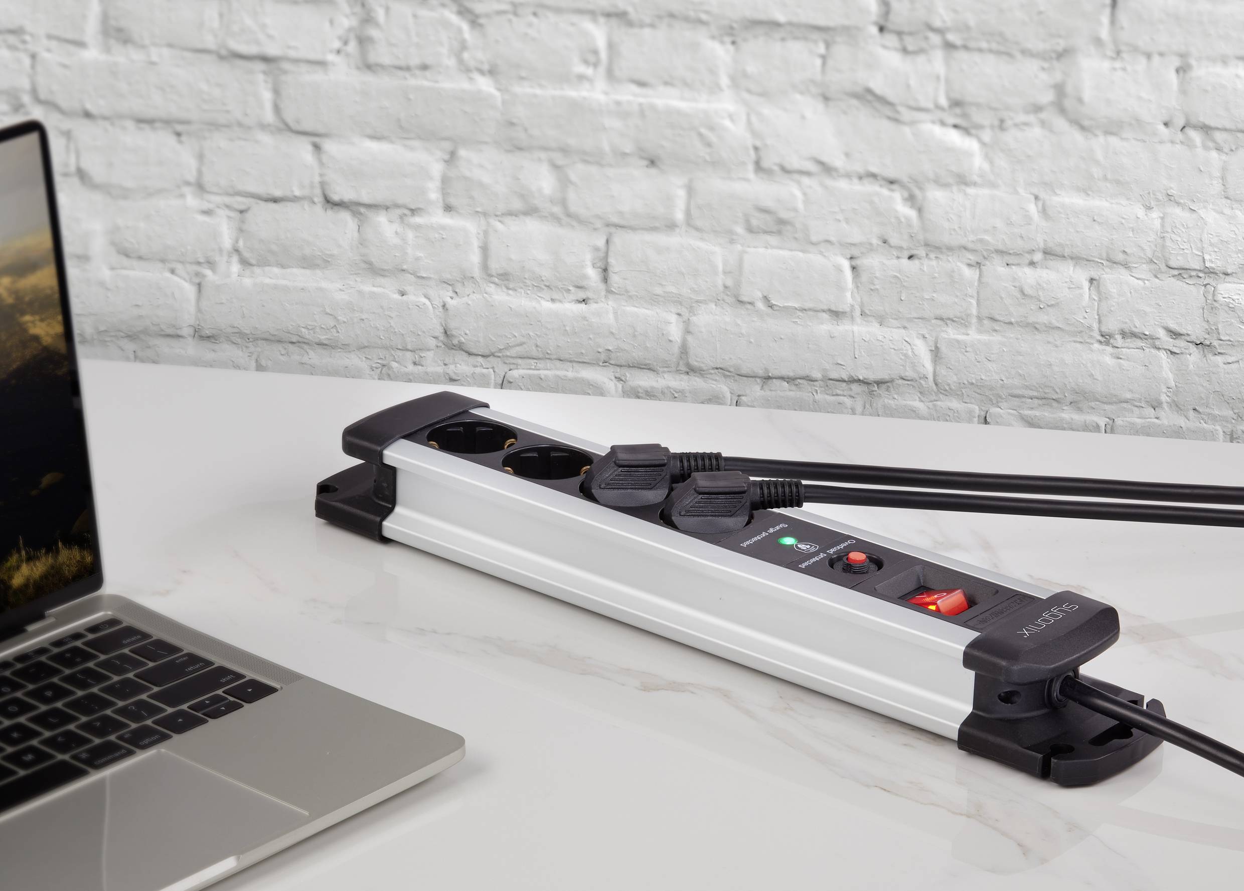 Mehrfachsteckdose mit mehreren Steckplätzen und eingebauten Schaltern auf einem Tisch. Ein Laptop ist daneben platziert.