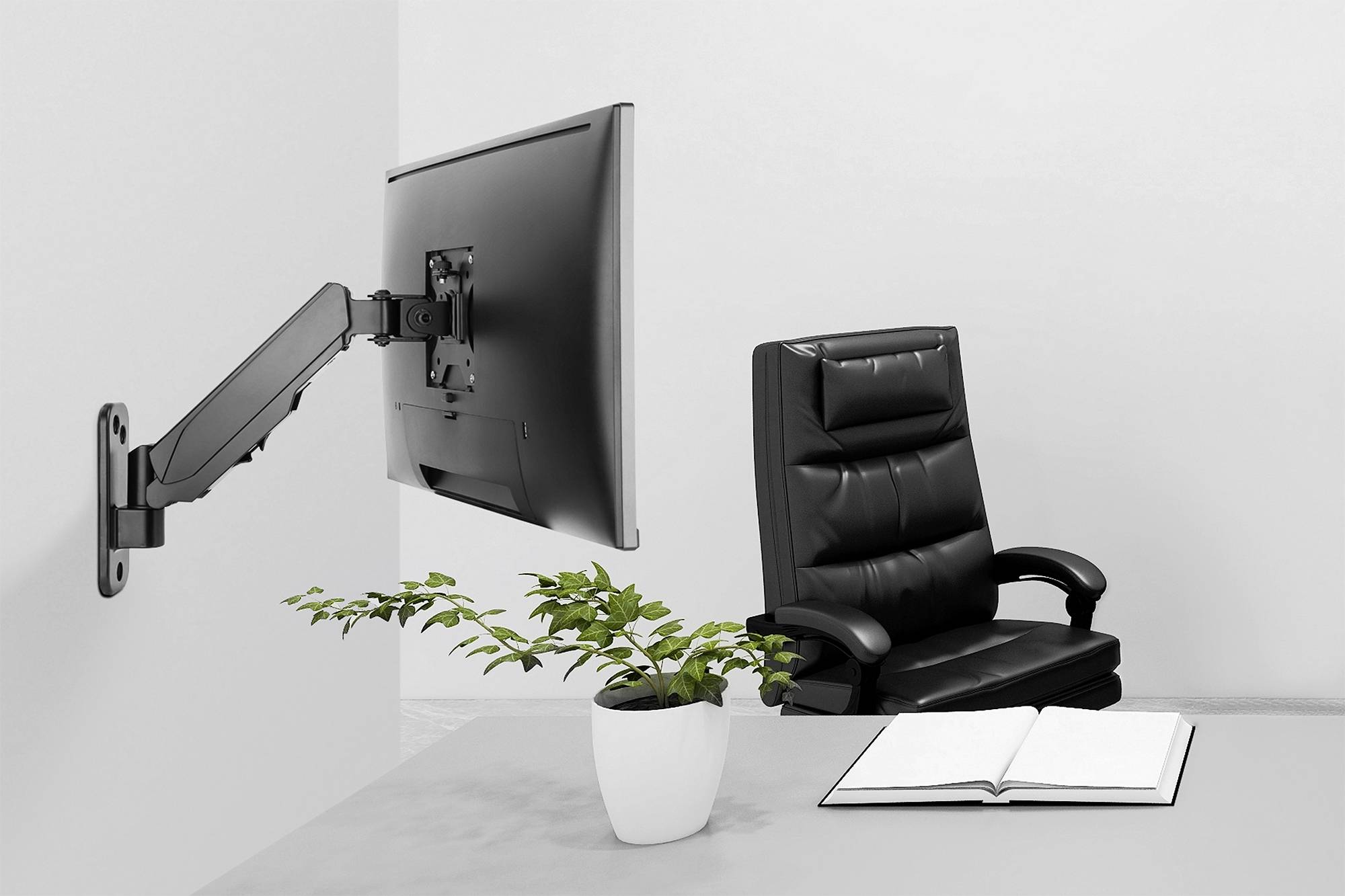 Ein leerer Schreibtisch mit offenem Buch und Topfpflanze. An der Wand ist ein Monitor an einem schwenkbaren Arm befestigt. Ein schwarzer Bürostuhl steht dahinter.