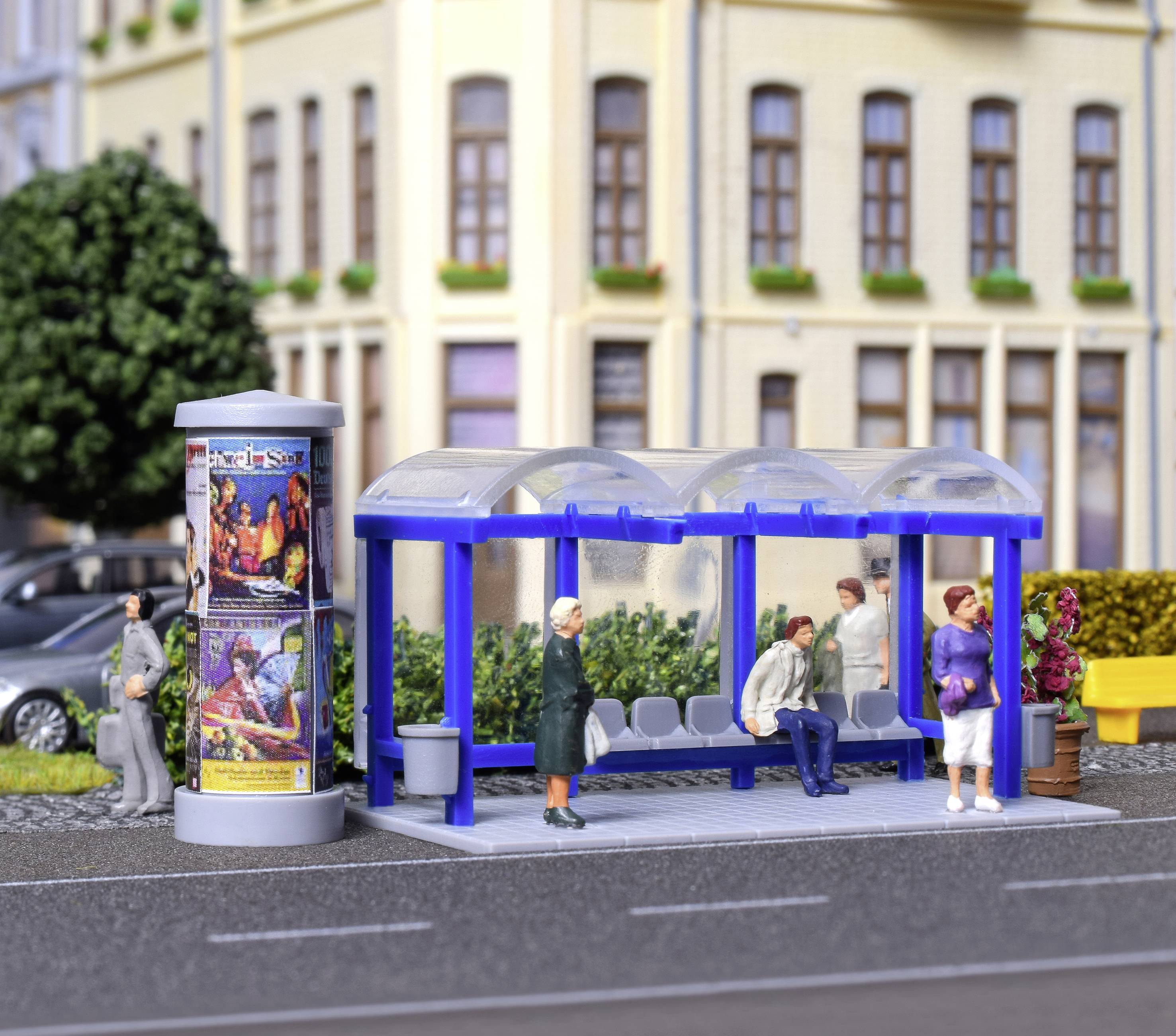 Bushaltestelle mit Personen: Zwei Personen stehen und zwei sitzen auf Bänken. Im Hintergrund ein Gebäude, daneben ein Plakatständer.