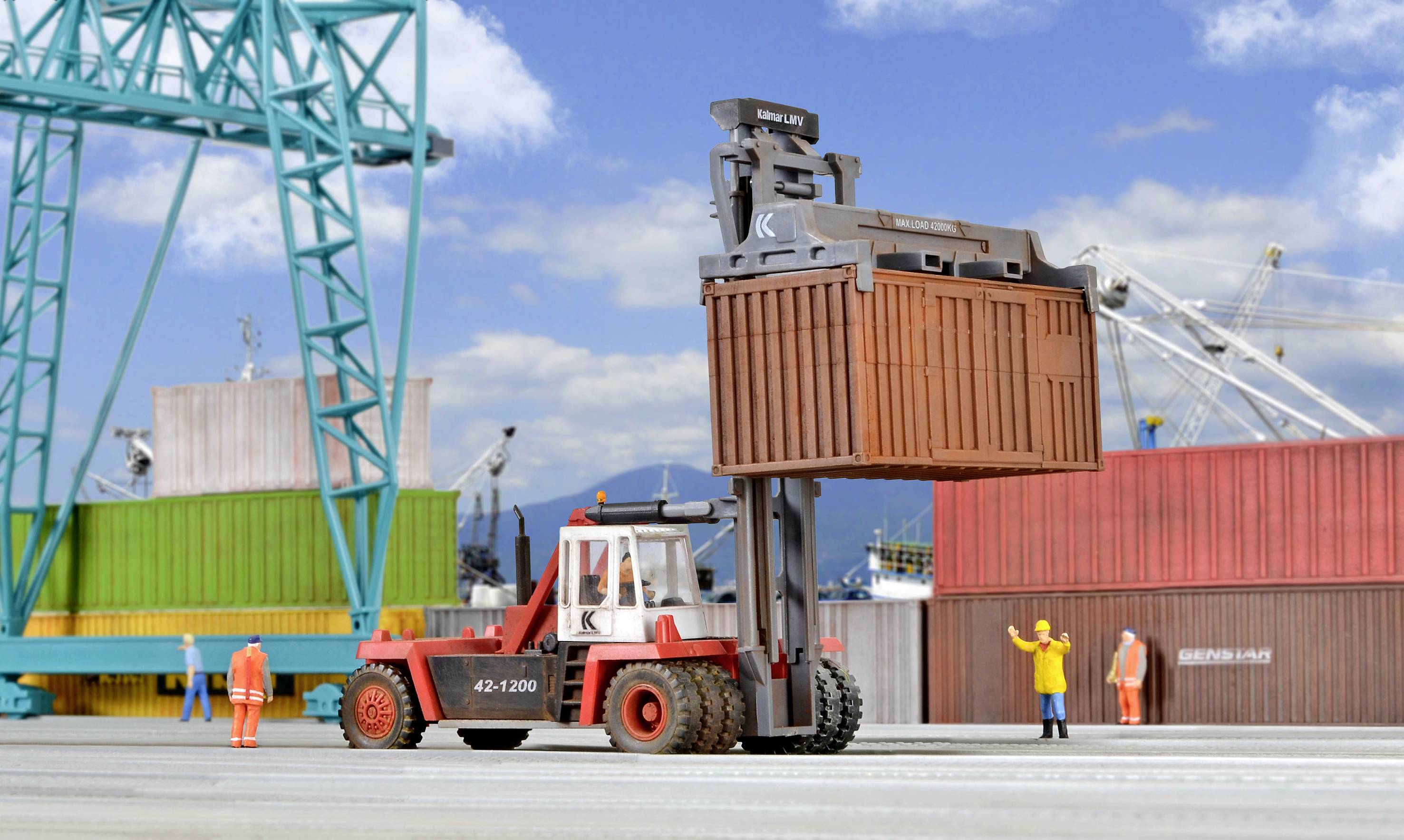 Ein Gabelstapler hebt einen Container im Hafen. Im Hintergrund sind Kräne, Container und mehrere Arbeiter zu sehen.