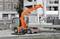 Ein LKW mit orangefarbenem Kran lädt Rohre von einer Baustelle ab. Im Hintergrund sind teilweise gebaute Gebäude zu sehen.