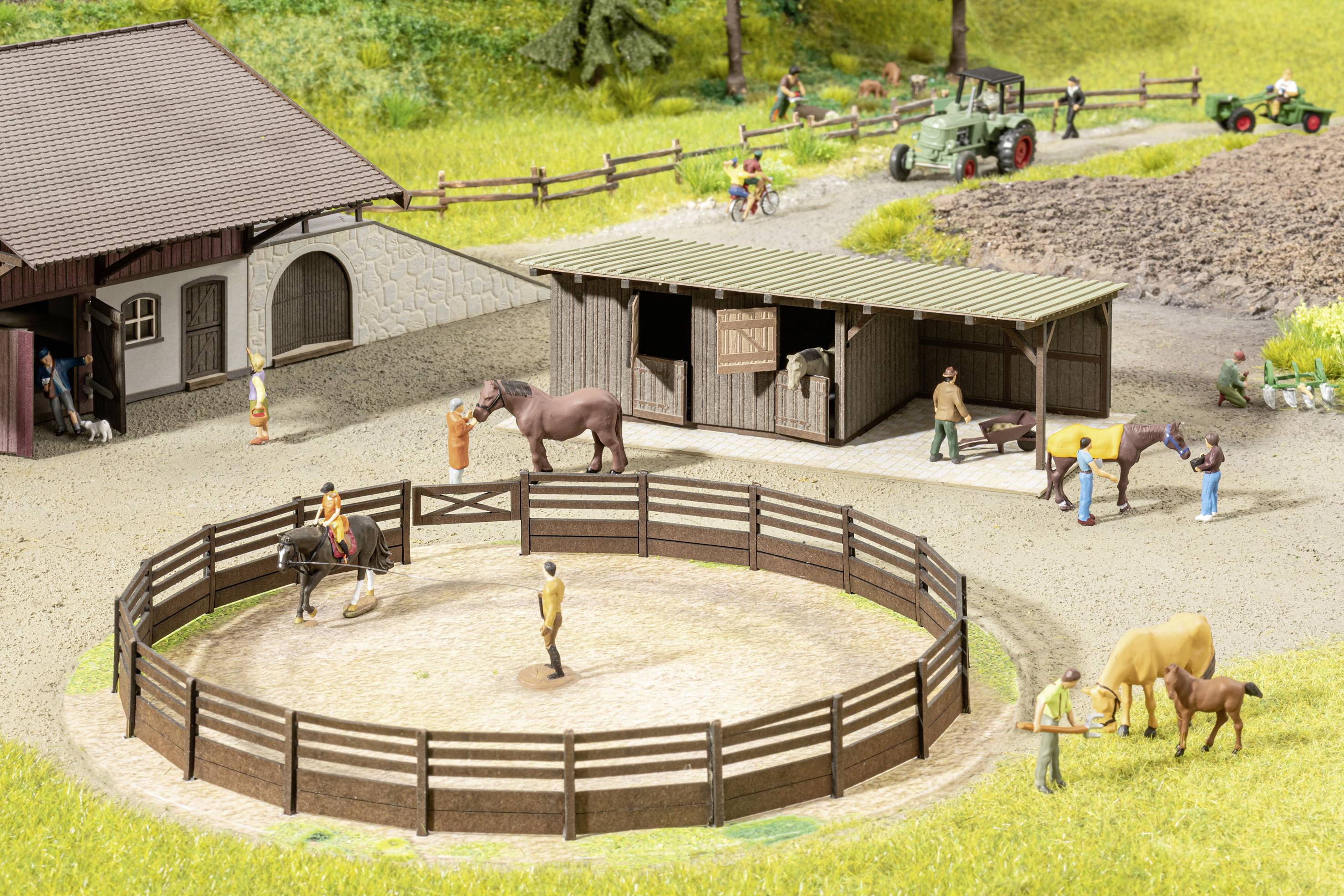 Ein Modellbau-Bauernhof zeigt Menschen und Pferde in einem Reitstall mit Koppel, Scheune, Gehege und Traktor auf einem Feld.