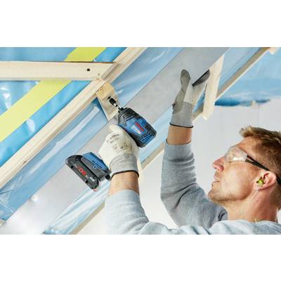 Ein Mann befestigt eine Metallstrebe an einer Decke mit einem blauen Akku-Bohrer. Er trägt Schutzbrille und Handschuhe.