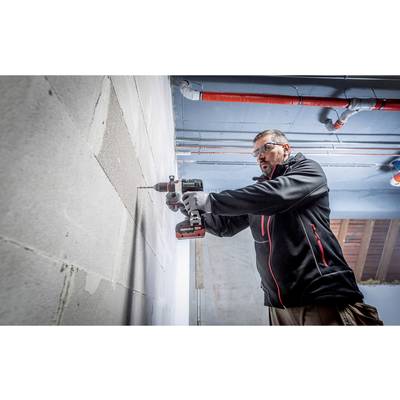 Eine Person mit Schutzbrille verwendet eine Bohrmaschine an einer Betonwand in einer Baustellenumgebung.