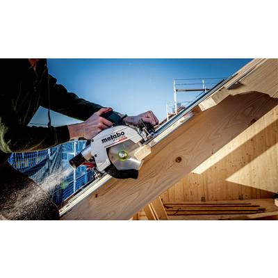 Eine Person arbeitet mit einer Handkreissäge auf einem Holzgerüst bei Tageslicht. Holzspäne fliegen von der Säge.