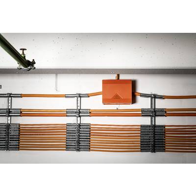 Orange Kabel verlaufen horizontal an einer Wand entlang, befestigt mit Metallklammern. Ein orangefarbener Anschlusskasten ist in der Mitte.