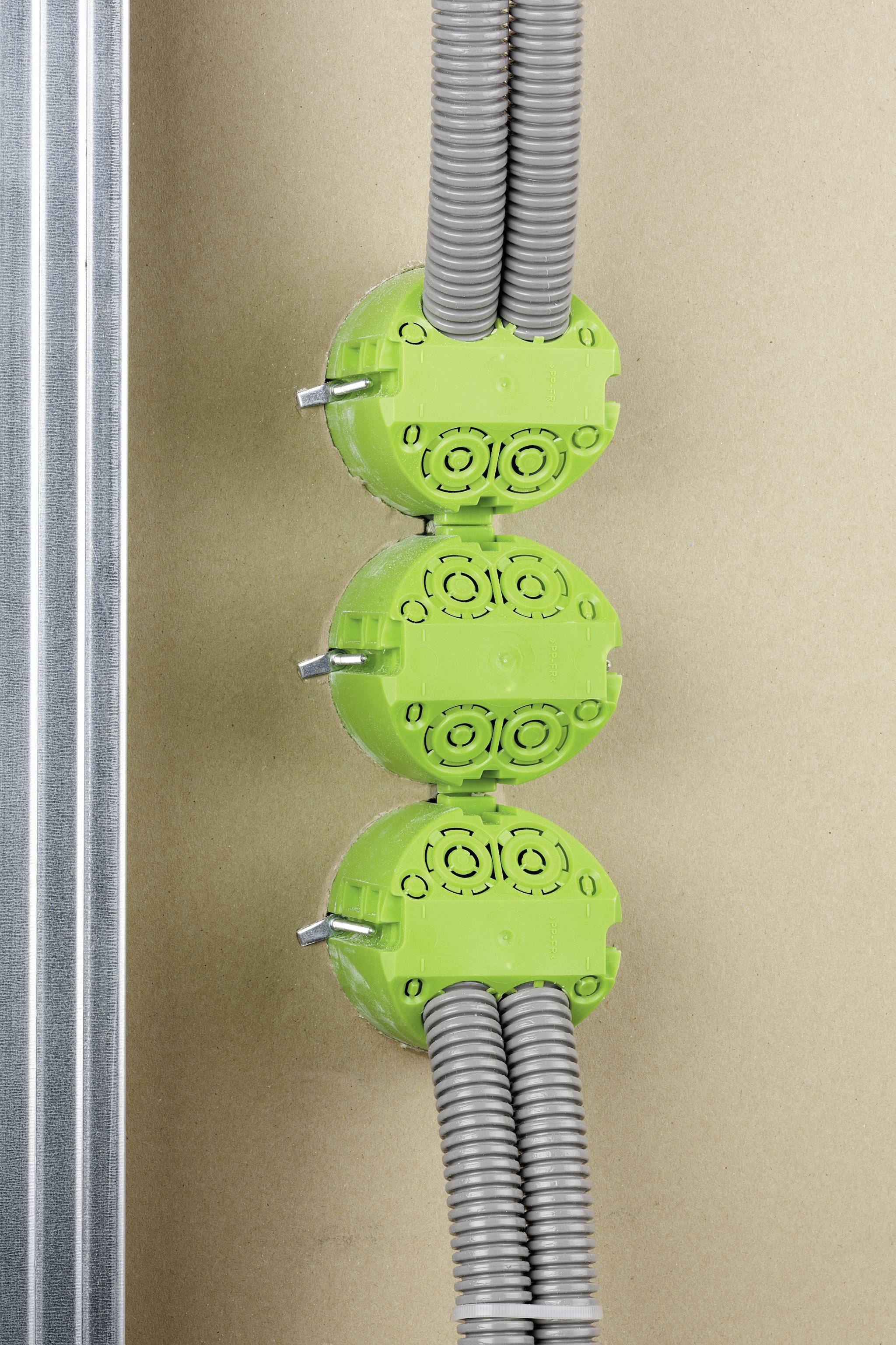 Drei grüne Elektroinstallationsdosen mit grauen Kabeln sind in einer Wand montiert, links befindet sich ein Metallträger.