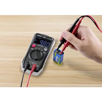 Eine Person misst die Spannung einer 9-Volt-Batterie mit einem Digitalmultimeter. Das Display zeigt 9,8 Volt an.
