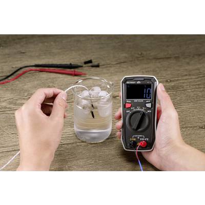 Eine Person misst mit einem Multimeter die elektrische Leitfähigkeit von Wasser in einem Glas mit Eiswürfeln. Die Anzeige zeigt '10' an.