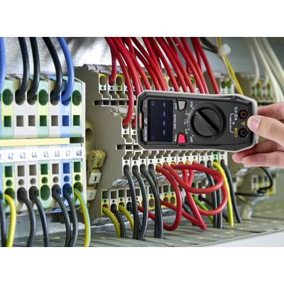 Eine Person verwendet ein Multimeter, um die Spannung in einem elektrischen Schaltschrank zu messen. Bunte Kabel sind angeschlossen.