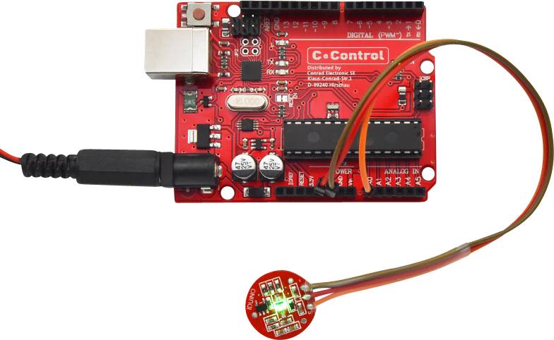 'Arduino-ähnliches Board mit Mikrocontroller und LED; rote Platine mit Anschlüssen und Kabel, LED leuchtet grün.'