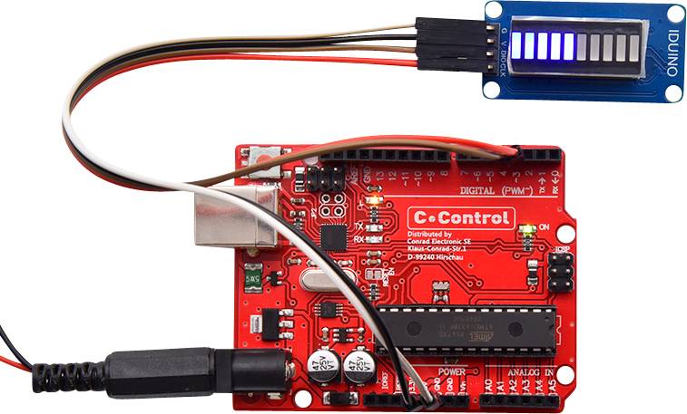 Rote elektronische Platine (C-Control), verbunden mit einem blauen LED-Display über Kabel. Hauptkomponenten und Anschlüsse sichtbar.