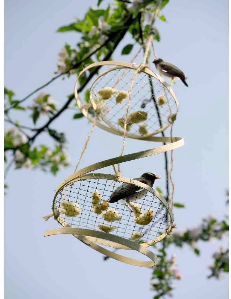Zwei Vögel sitzen auf einem dekorativen, mit Blumen bestückten Gitter, das an einem blühenden Ast hängt; klarer Himmel im Hintergrund.