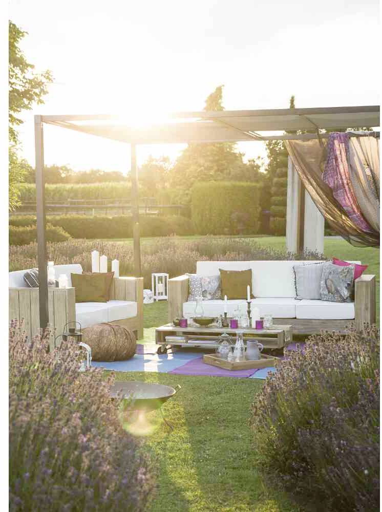 Gemütlicher Outdoor-Sitzbereich bei Sonnenuntergang, mit weißen Sofas, Kissen und dekorativen Elementen auf einem grünen Rasen.