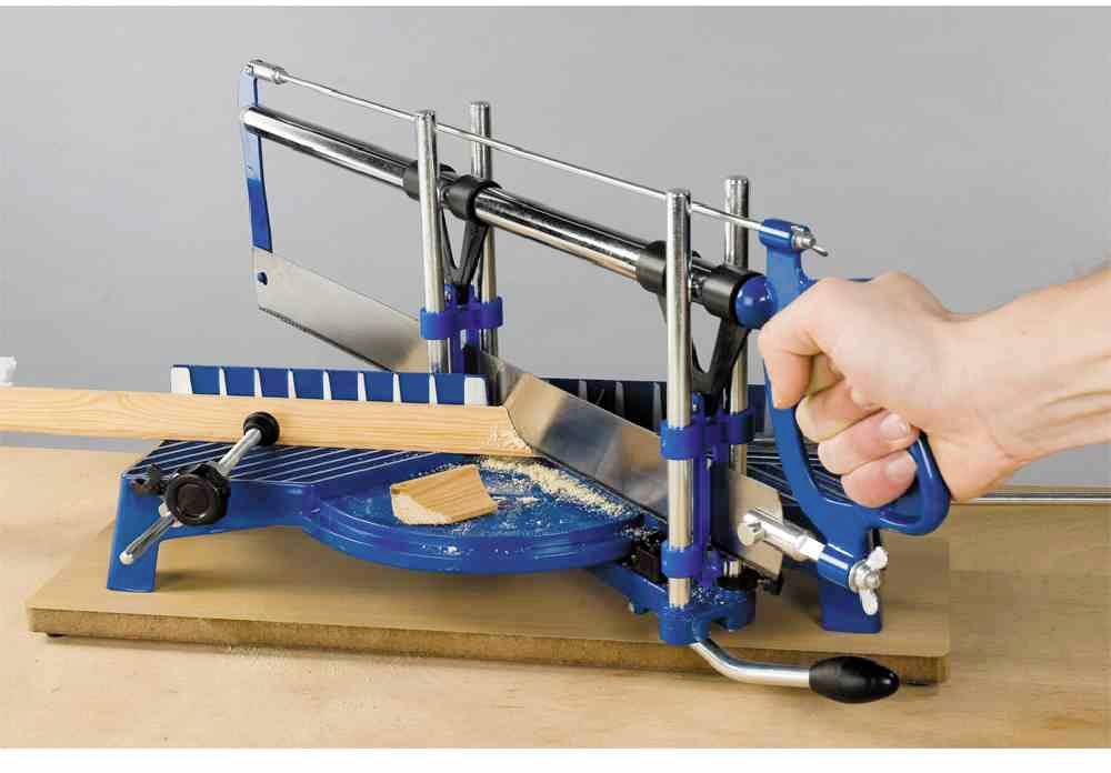 Eine Hand sägt mit einer Gehrungssäge einen Holzstab auf einem Tisch, umgeben von blauen Metallschienen zur Führung der Säge.