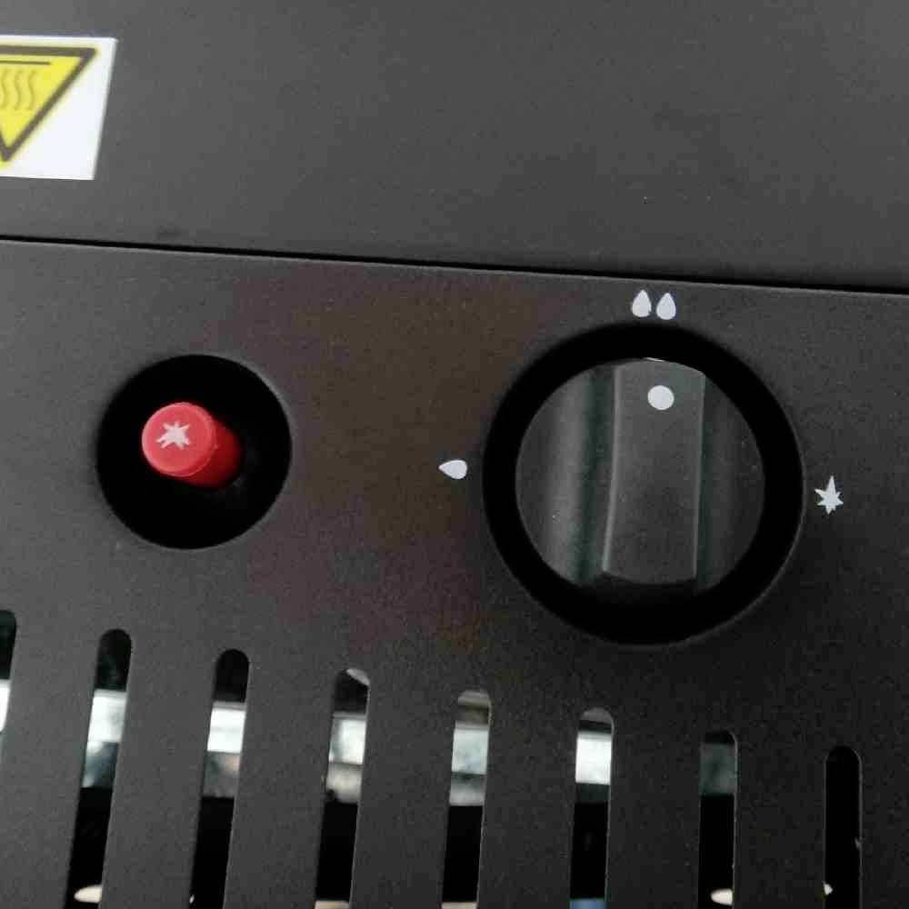 Schwarz-graues Bedienfeld mit rotem Knopf links und transparentem Drehschalter rechts, umgeben von Tropfen- und Sternsymbolen.