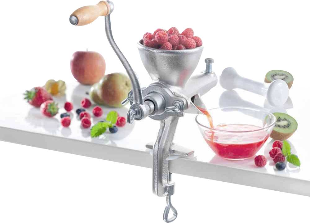Frisch gepresster Himbeersaft tropft aus einer handbetriebenen Saftpresse. Frische Himbeeren, ein Apfel und Kiwi liegen daneben.