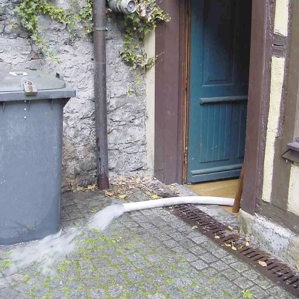 Ein grauer Müllcontainer steht nahe einer Hauswand, aus dem Wasser über eine Kante auf ein gepflastertes Gelände fließt.