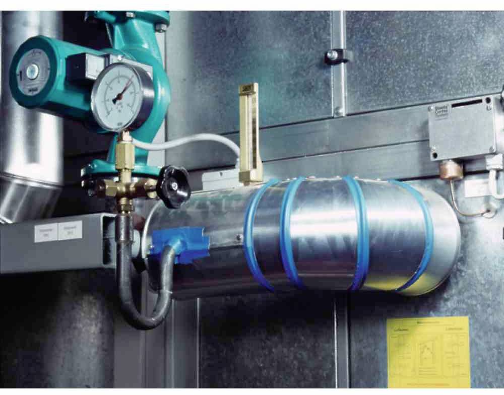 Ein metallisches Rohrsystem mit Druckanzeige und Ventilen vor einer schweren Metallwand. Ein gelbes Dokument ist an der Wand befestigt.