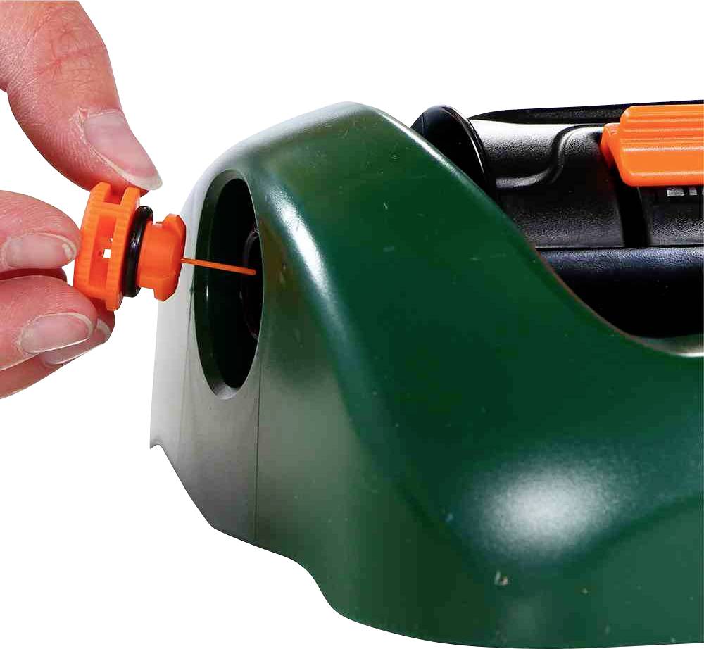 Eine Hand setzt eine orangefarbene Ersatz-Zündkerze in ein grünes Gerät ein, das möglicherweise ein Rasenmäher ist.