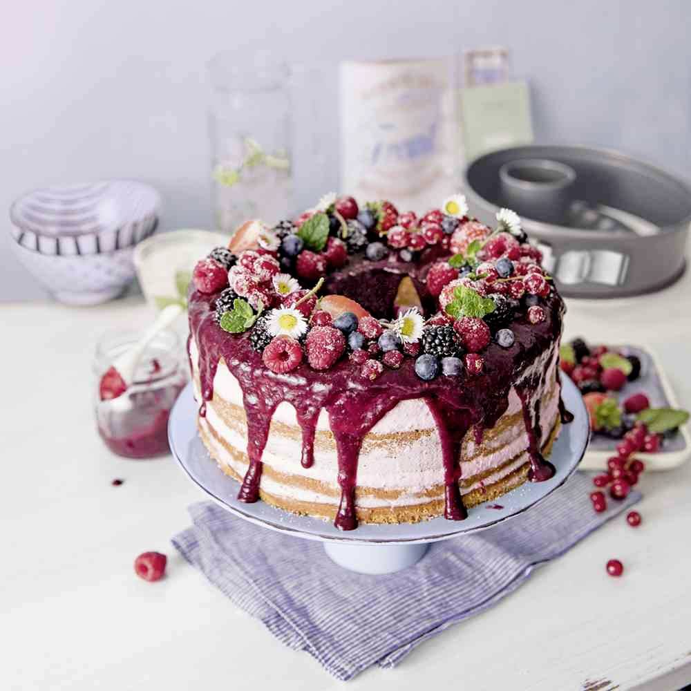 Ein großer, dekorierter Kuchen mit roten Beeren und Sahne auf einem blauen Kuchenteller. Dekoration aus Himbeeren, Heidelbeeren, Johannisbeeren und Minzblättern.