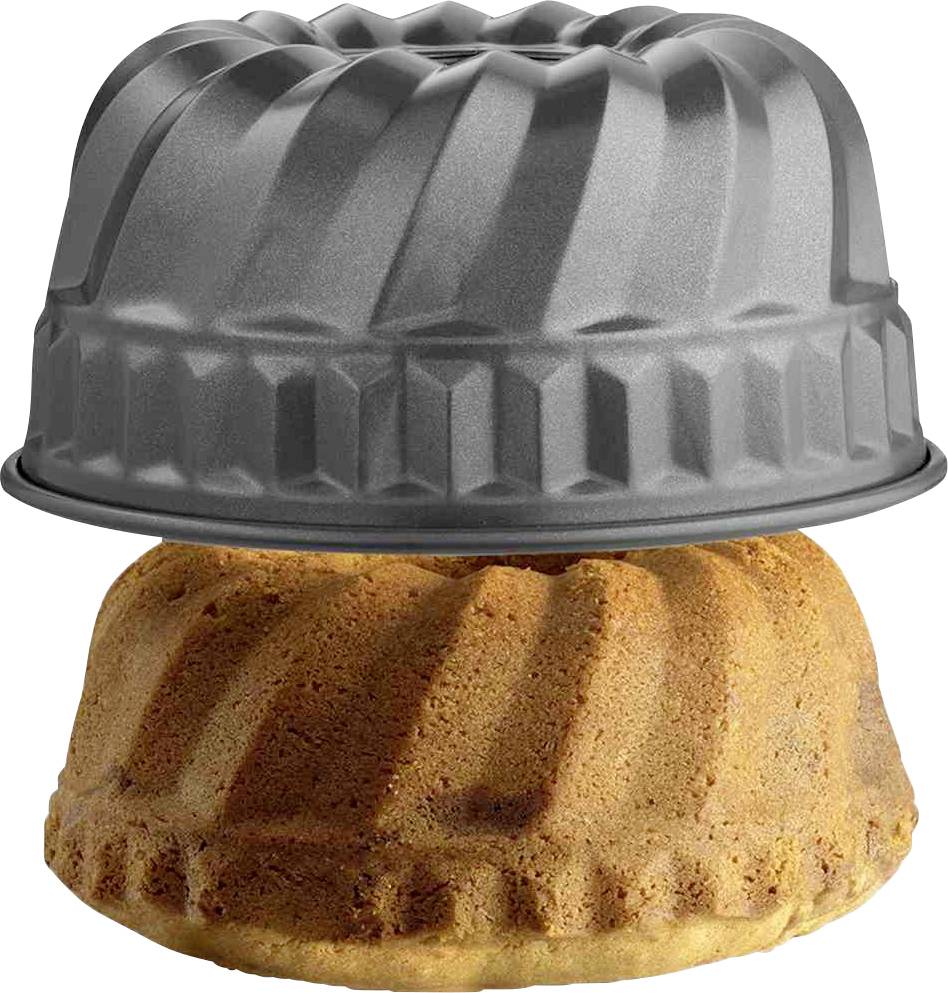 Eine graue Gugelhupf-Backform ruht auf einem frisch gebackenen Gugelhupf-Kuchen. Der Kuchen ist goldbraun und hat dasselbe Muster wie die Form.