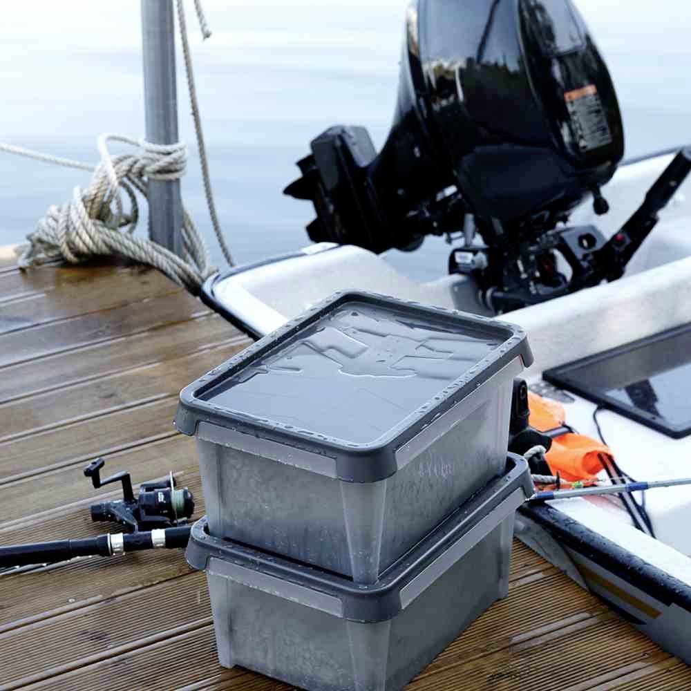Boxen mit Abdeckung gefüllt mit Köderfischen stehen auf einem Bootssteg neben einem festgebundenen Boot.