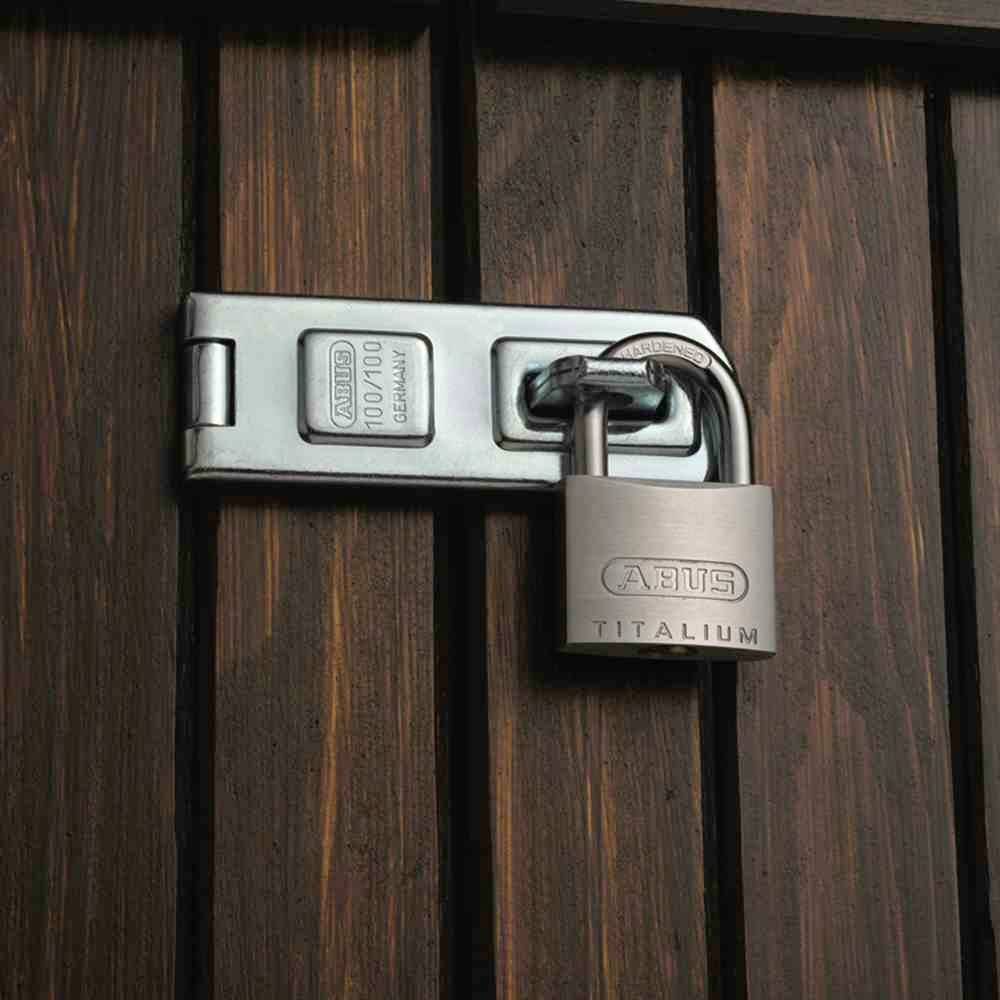 Ein Vorhängeschloss sichert eine Holztür. Auf dem Schloss steht 'ABUS Titalium'. Das Schloss symbolisiert Sicherheit.