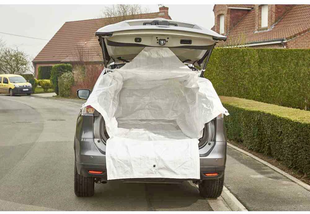 Auto mit geöffneter Heckklappe auf einer Straße. Ein großes weißes Tuch bedeckt den Innenraum des Kofferraums. Wohnhäuser im Hintergrund.
