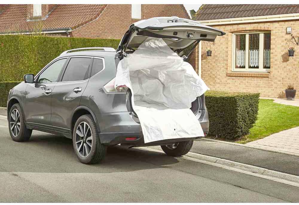 Ein grauer SUV parkt vor einem Backsteinhaus. Der Kofferraum ist geöffnet und mit einer hellen Plane ausgekleidet. Links ist ein gepflegter Garten.