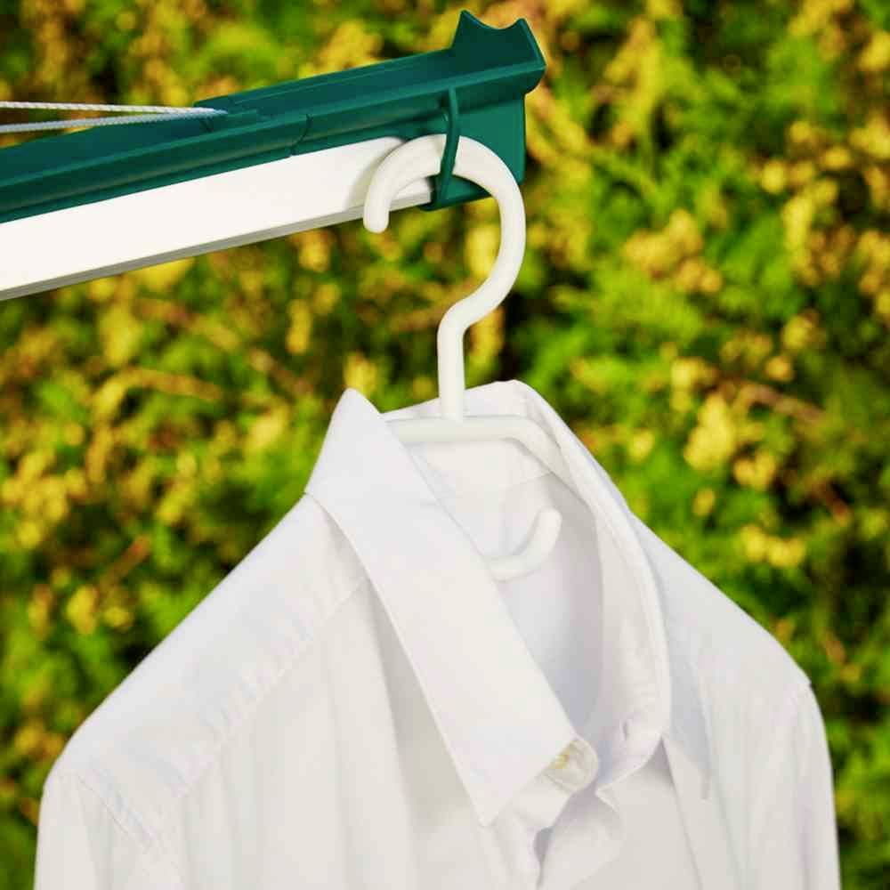 Ein weißes Hemd hängt auf einem Kleiderbügel an einer Wäscheleine vor einem Hintergrund aus grünen Büschen.